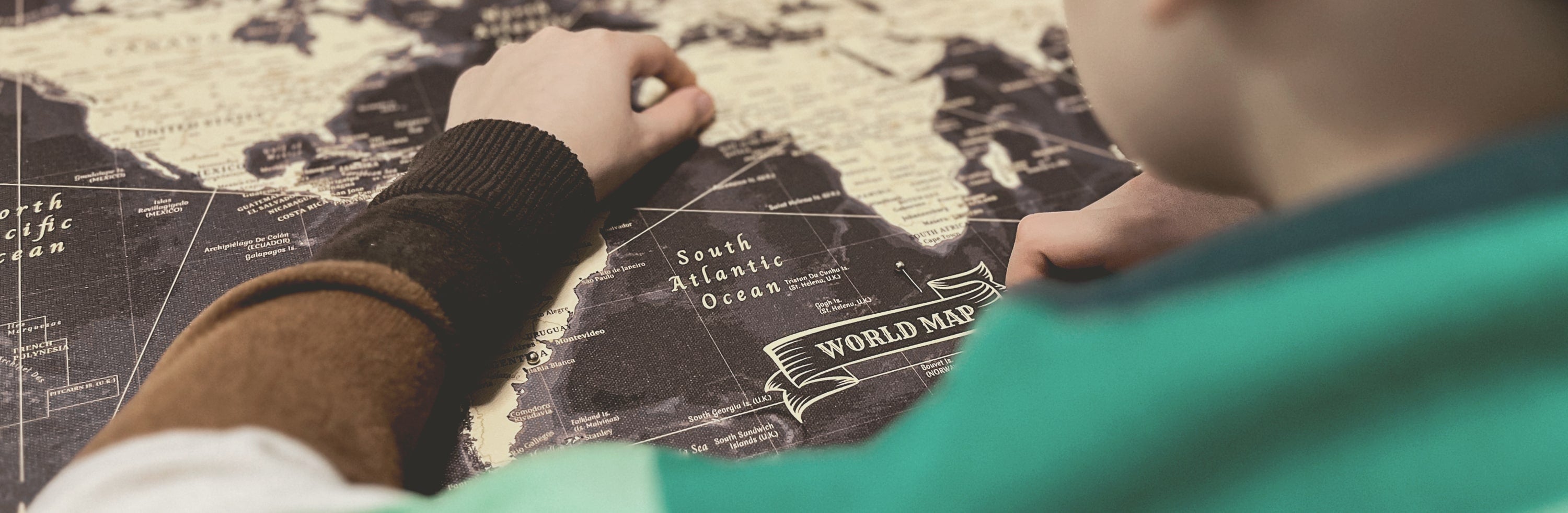 Close-up view of a young individual pinpointing a destination on a stylish world map canvas with push pins, perfect for wall art and tracking travel adventures – available as a world map pin board from www.pinmap.eu for avid explorers and travel enthusiasts.