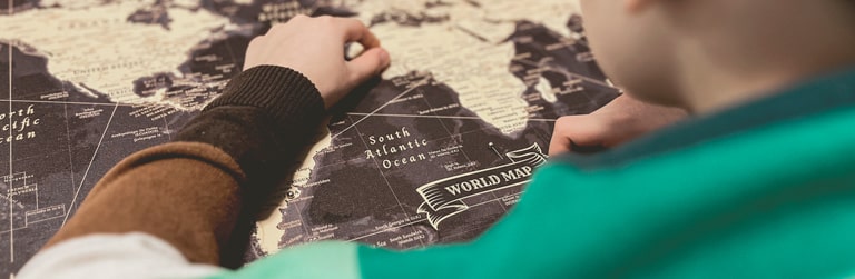 Close-up view of a young individual pinpointing a destination on a stylish world map canvas with push pins, perfect for wall art and tracking travel adventures – available as a world map pin board from www.pinmap.eu for avid explorers and travel enthusiasts.