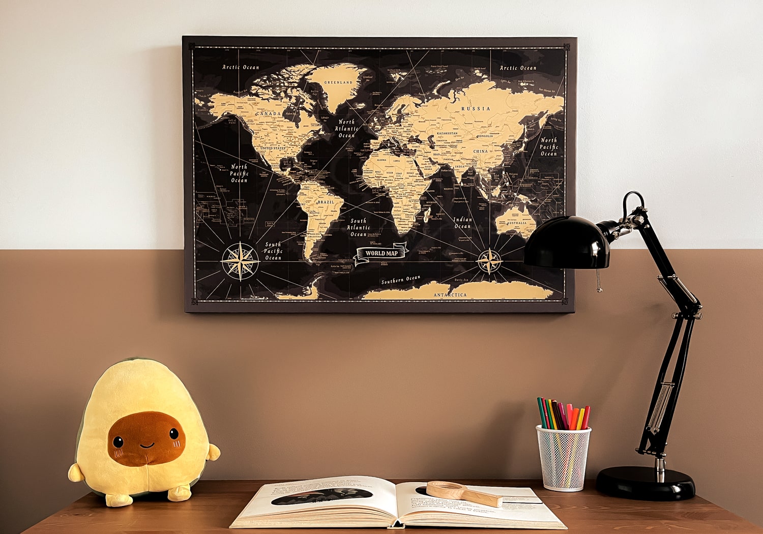 Ein gut organisiertes Arbeitszimmer mit einer Vintage Weltkarte Pinnwand in Schwarz und Gold an der Wand, begleitet von einem Plüsch-Avocado-Spielzeug, einer Leselampe und buntem Schreibwaren, inspirierend für Reiseplanung und Lernen.