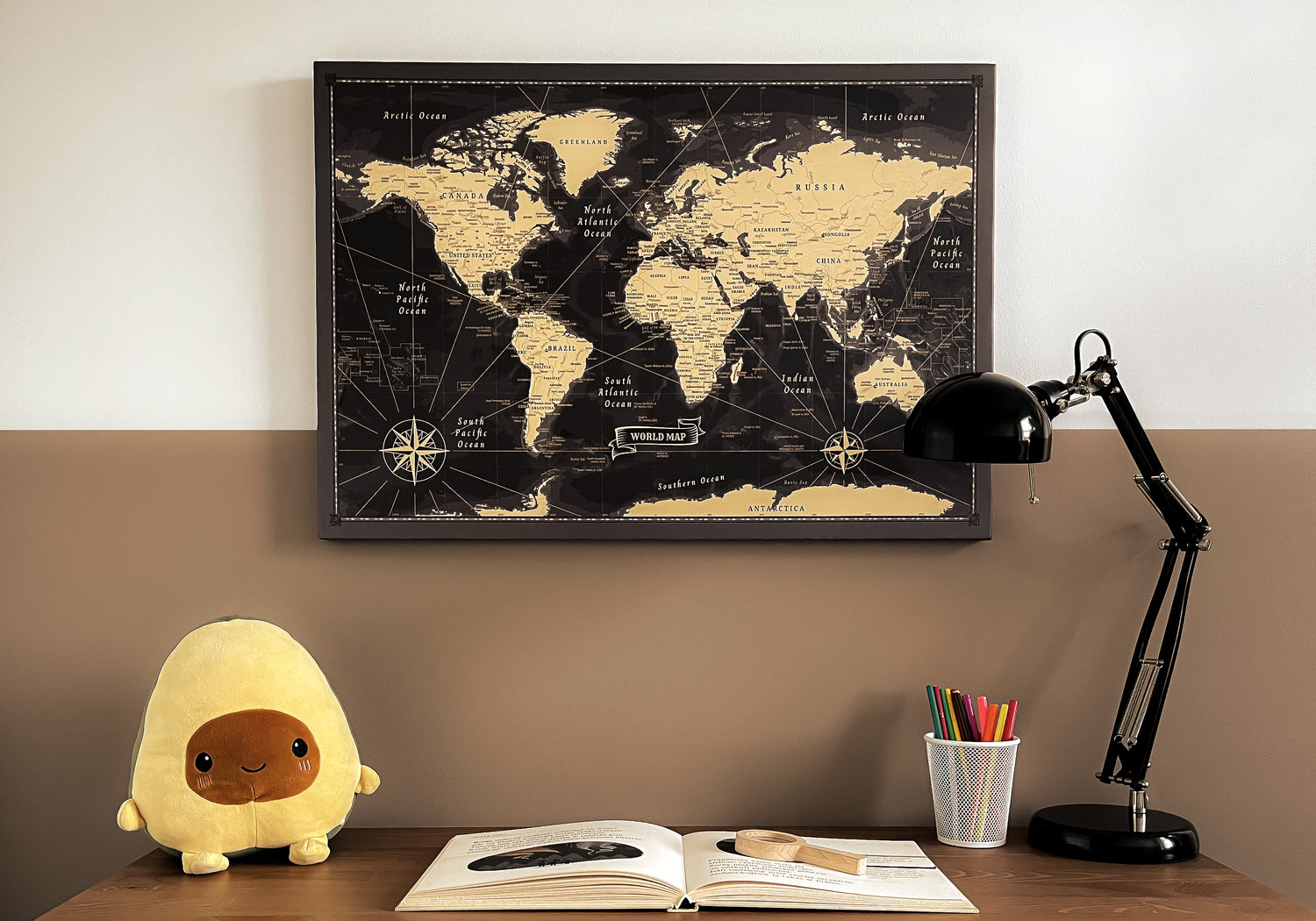 A well-organized study space with a vintage black and gold world map pinboard on the wall, accompanied by a plush toy avocado, a reading lamp, and colorful stationery, ideal for inspiring travel planning and educational exploration.