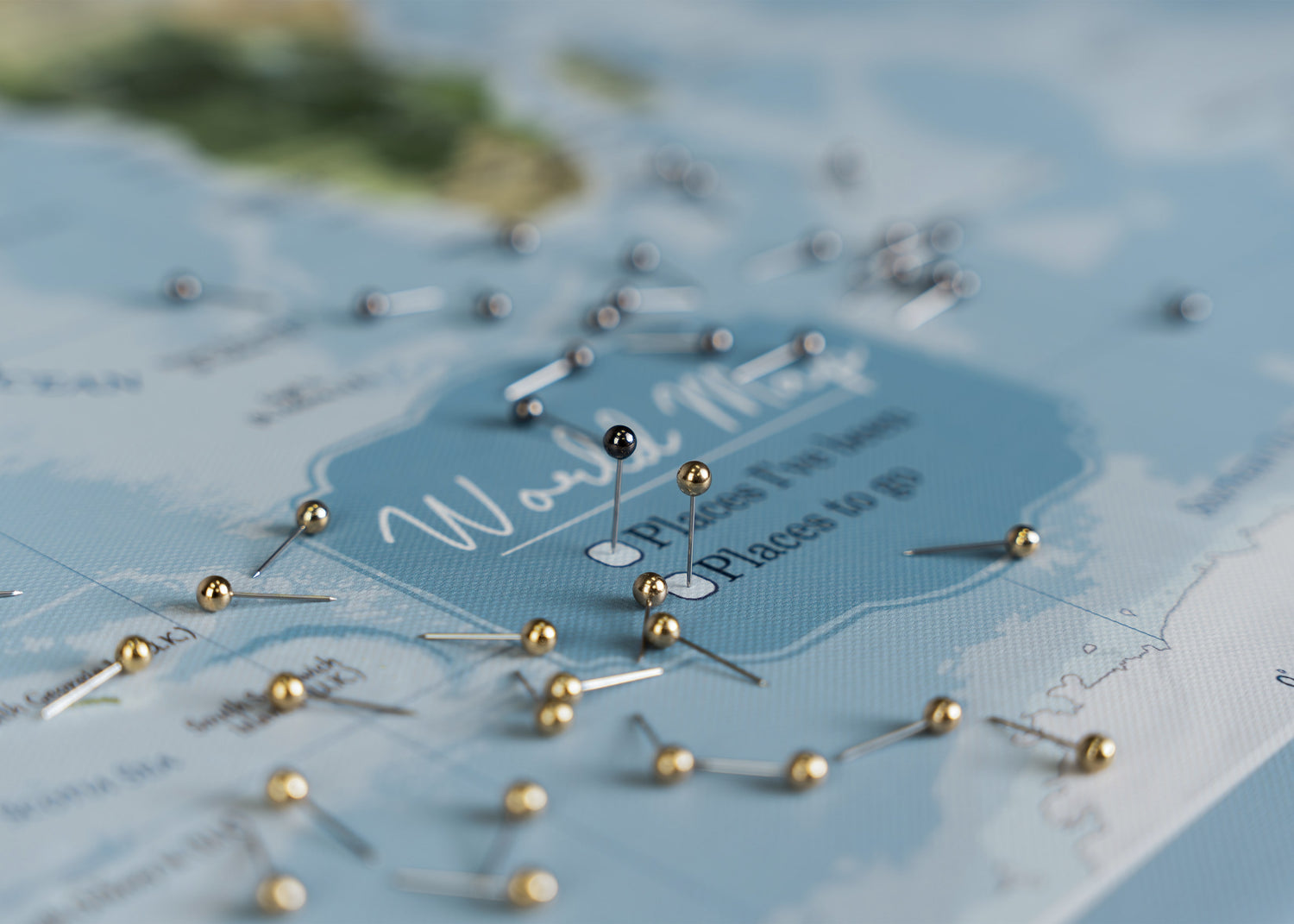 Close-up of a light blue world map pinboard with gold and black pins highlighting travel destinations, an inspiring gift for travelers to capture their journeys and plan future explorations.